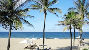 A beach with palm trees, lounge chairs, and umbrellas. - Mai Villa & Apartment (Da Nang)