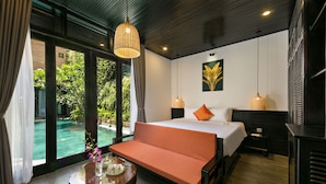 A hotel room with a bed, a sofa, a table with a vase, and a view of a swimming pool. - Mai Villa & Apartment (Da Nang)