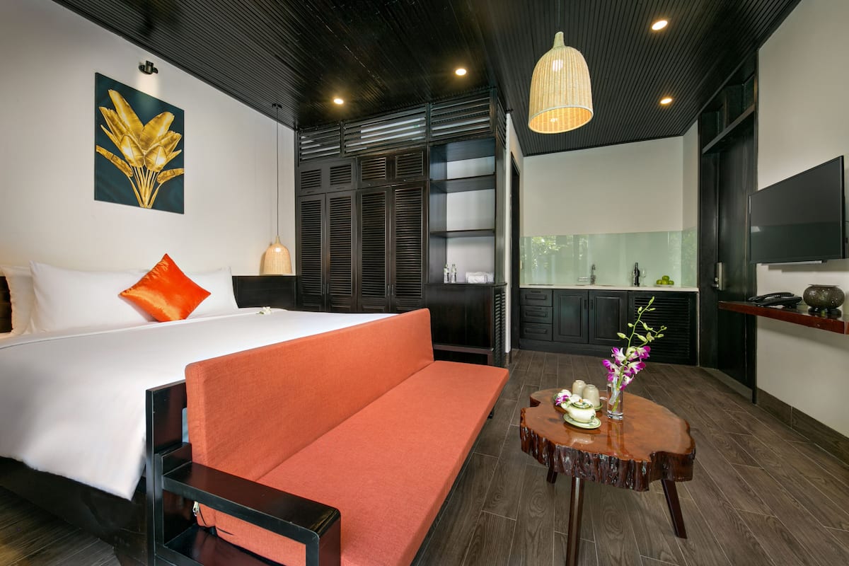 Ein modernes Hotelzimmer mit Bett, orangefarbenem Sofa, Holztisch mit einer Vase und einem an der Wand befestigten Fernseher.
