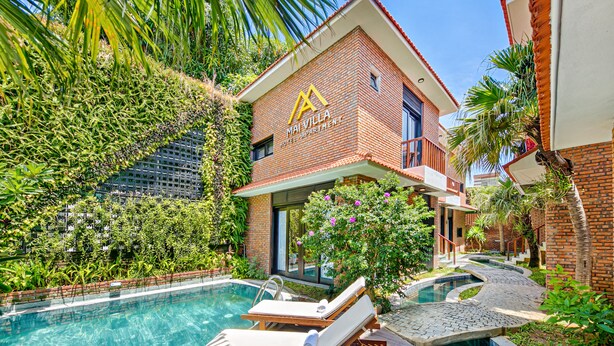 A hotel with a swimming pool, lounge chairs, and lush greenery. - Mai Villa & Apartment (Da Nang)