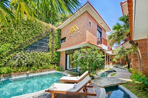 A hotel with a swimming pool, lounge chairs, and lush greenery. - Mai Villa & Apartment (Da Nang)
