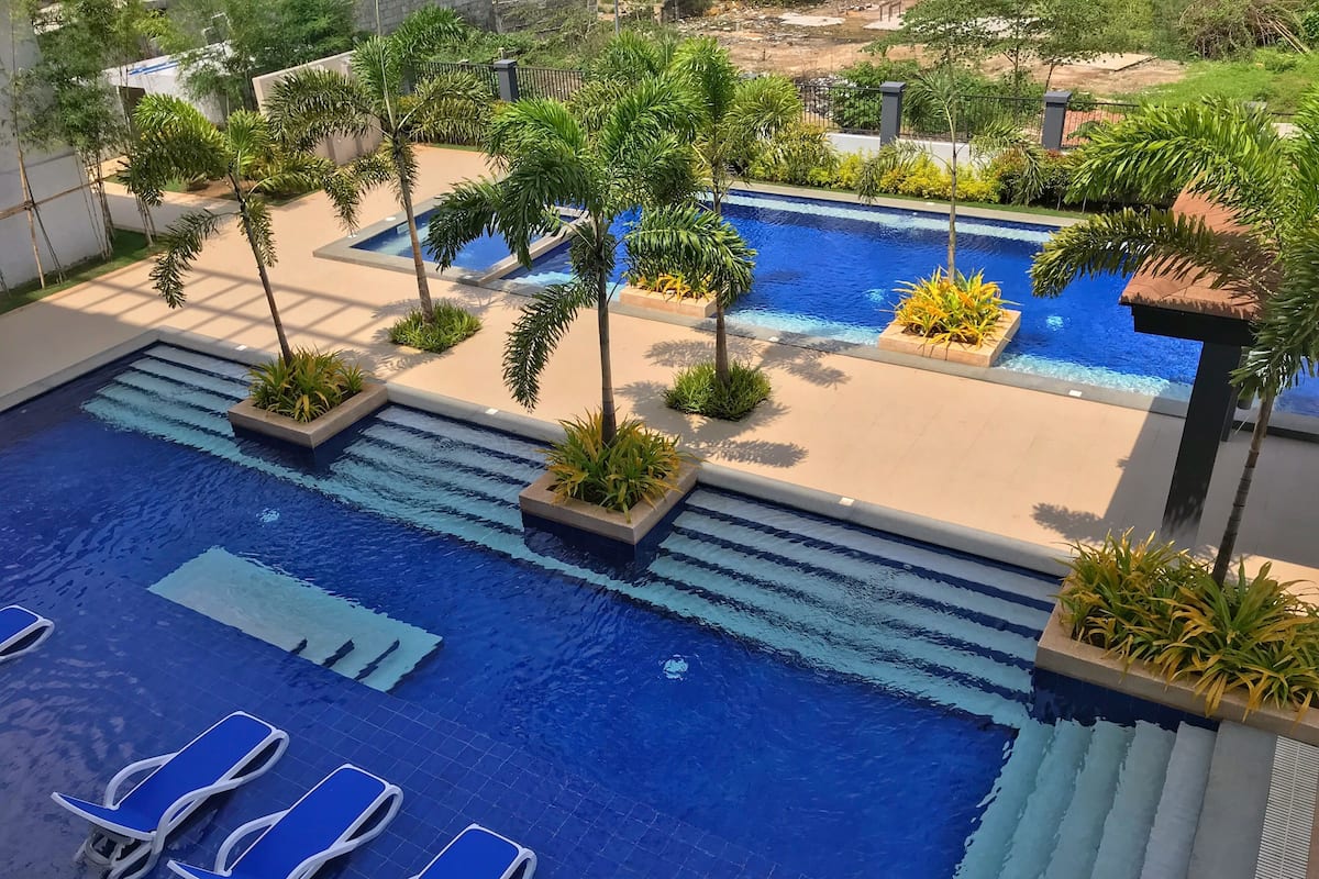 Una piscina con agua azul, rodeada de palmeras y plantas, y sillas de descanso azules.