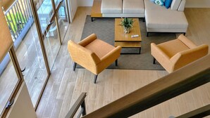 A modern living room with a sofa, two armchairs, a coffee table, and a staircase.
