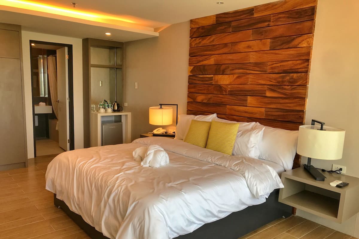 Habitación de hotel con una cama grande, cabecera de madera, mesita de noche con lámpara y un espejo.
