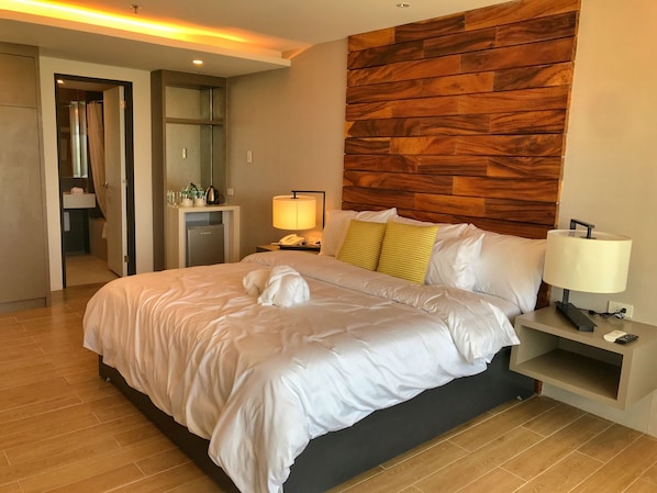 Une chambre d’hôtel avec un grand lit, une tête de lit en bois, une table de chevet avec une lampe et un miroir.