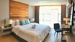 A hotel room with a large bed, two bedside tables with lamps, a chair, a TV, and a wooden accent wall.