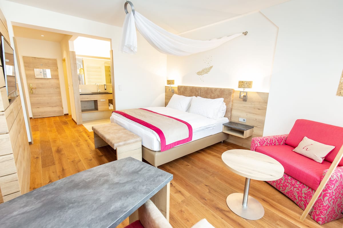 Una habitación de hotel moderna con una cama, un sofá rojo, una mesita y suelo de madera.