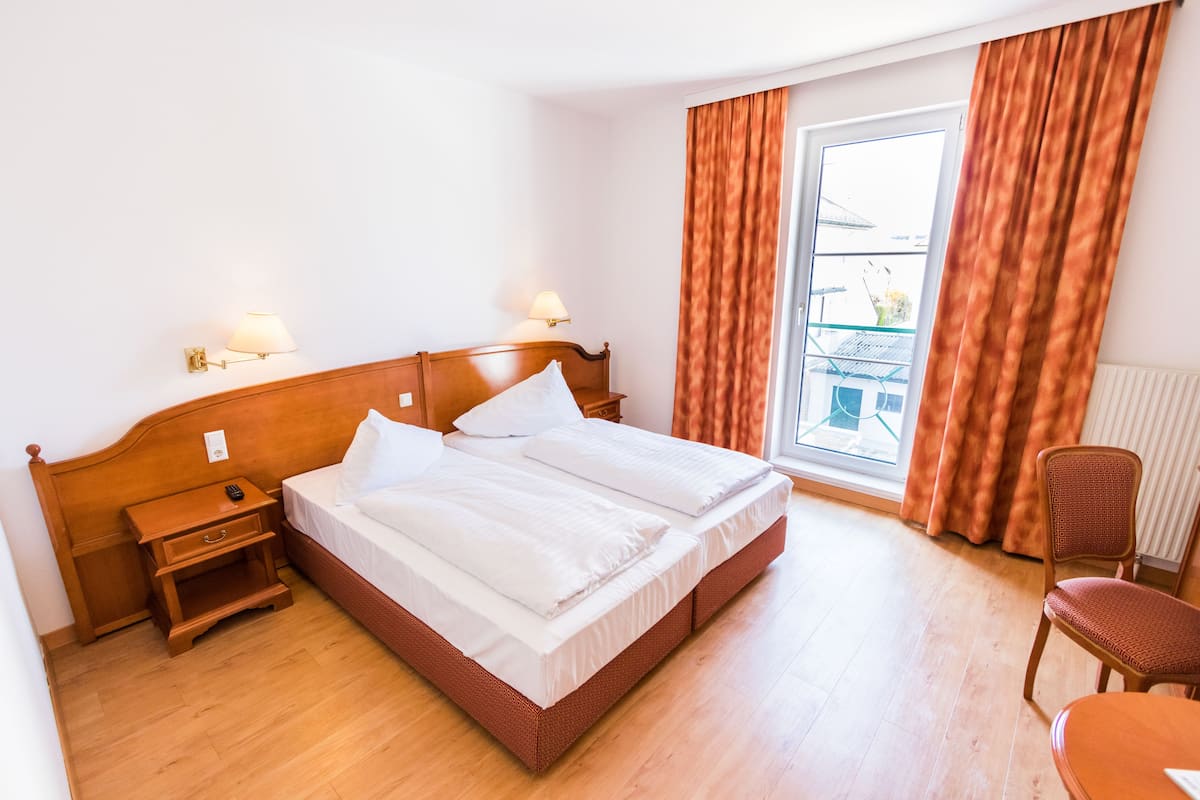 Una habitación de hotel con una cama de madera, mesitas de noche, una silla y una ventana con cortinas.