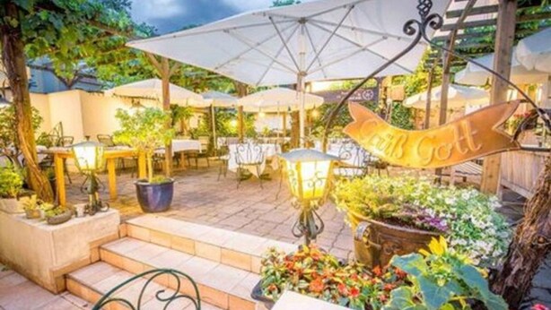 Un patio al aire libre con mesas y sombrillas, rodeado de plantas y flores en macetas.
