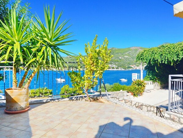 Une terrasse agrémentée de plantes en pot, dotée d’un sol carrelé et offrant une vue sur la mer et les bateaux.