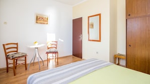Une chambre à coucher comprenant un lit, deux chaises en bois, une petite table, un miroir et une armoire.