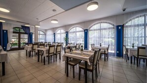 Un amplio comedor con varias mesas y sillas, ventanas grandes con cortinas e iluminación en el techo.