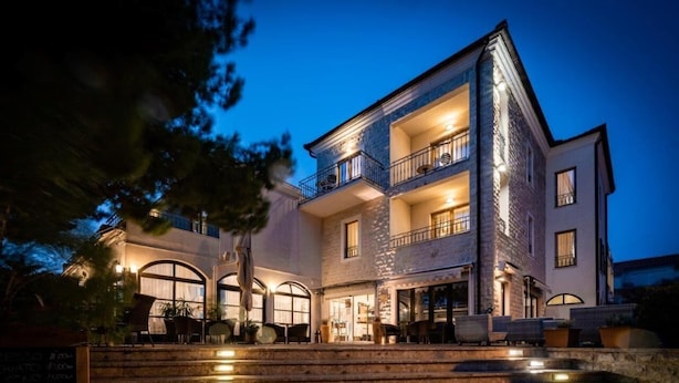 Un edificio de varios pisos con fachada de piedra, zona de estar al aire libre y ventanas iluminadas.