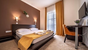 Una habitación de hotel con cama, escritorio, silla, televisor y ventana con cortinas.