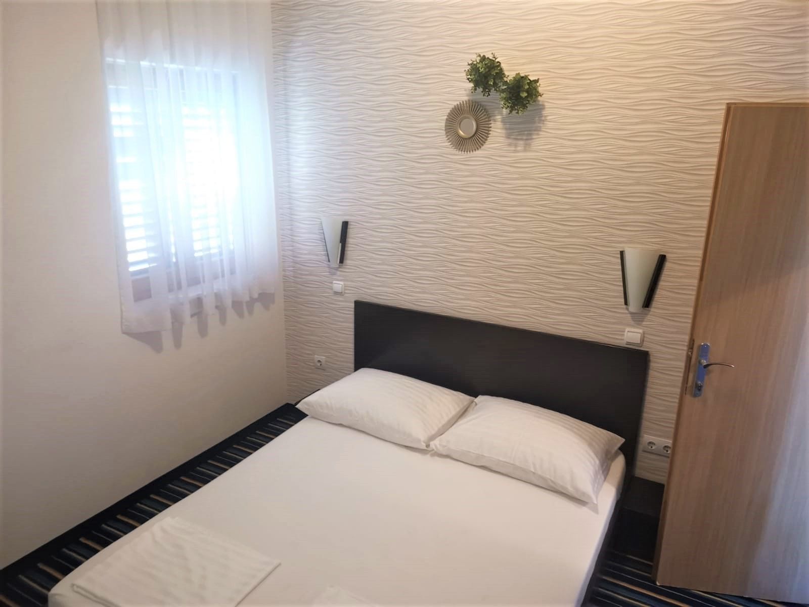 A hotel room with a bed, a window with curtains, a wall-mounted plant, and a door.