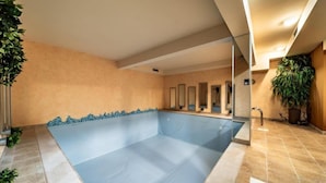 Una amplia piscina interior con revestimiento azul, rodeada de paredes beige y suelo de baldosas.