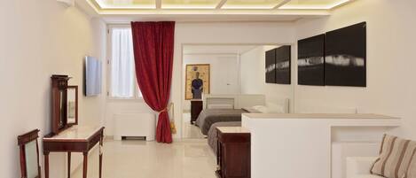 A modern hotel room with a large bed, a sitting area with a sofa and armchairs, a dining table, and artwork on the walls.