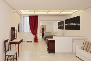 Una habitación de hotel moderna con una cama grande, una zona de estar con sofá y sillones, una mesa de comedor y obras de arte en las paredes.