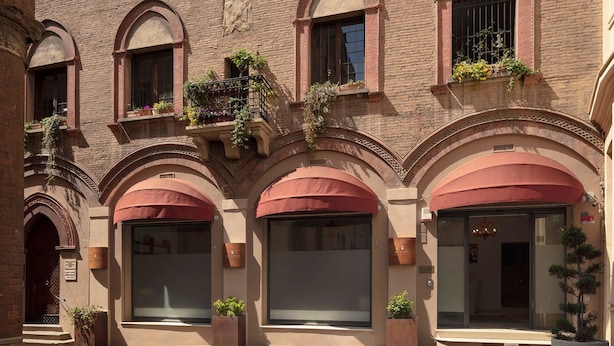 Un edificio con ventanas arqueadas y balcones con plantas. Se observan ventanas y puertas amplias, y la fachada es de ladrillo.