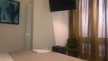 A hotel room with a bed, a flat-screen TV mounted on the wall, a chair, and a window with curtains.