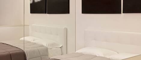 A hotel room with two beds, each with a white headboard and a beige quilted bedspread.