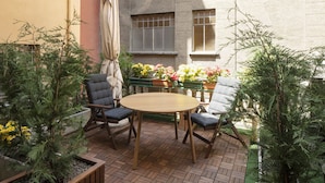 Un patio con una mesa redonda de madera y cuatro sillas, rodeado de plantas en macetas y un suelo de ladrillo.