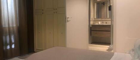A bedroom with a bed, a white bedside table, a nightstand, and a wardrobe.
