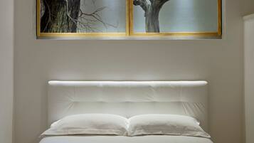 A bed with white bedding and a headboard, positioned under a framed artwork of a tree.