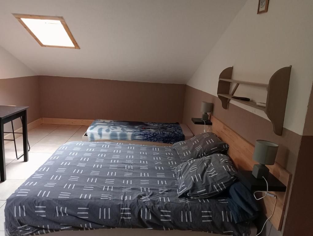 A small, single-room apartment with a sloped ceiling, a bed with a patterned bedspread, a desk, and a wall-mounted shelf.