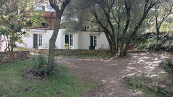 Un edificio blanco con base de piedra, rodeado de árboles y un área con césped.