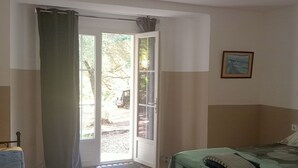 Un dormitorio con una cama, una silla, una puerta que da al exterior y una lámpara en el techo.