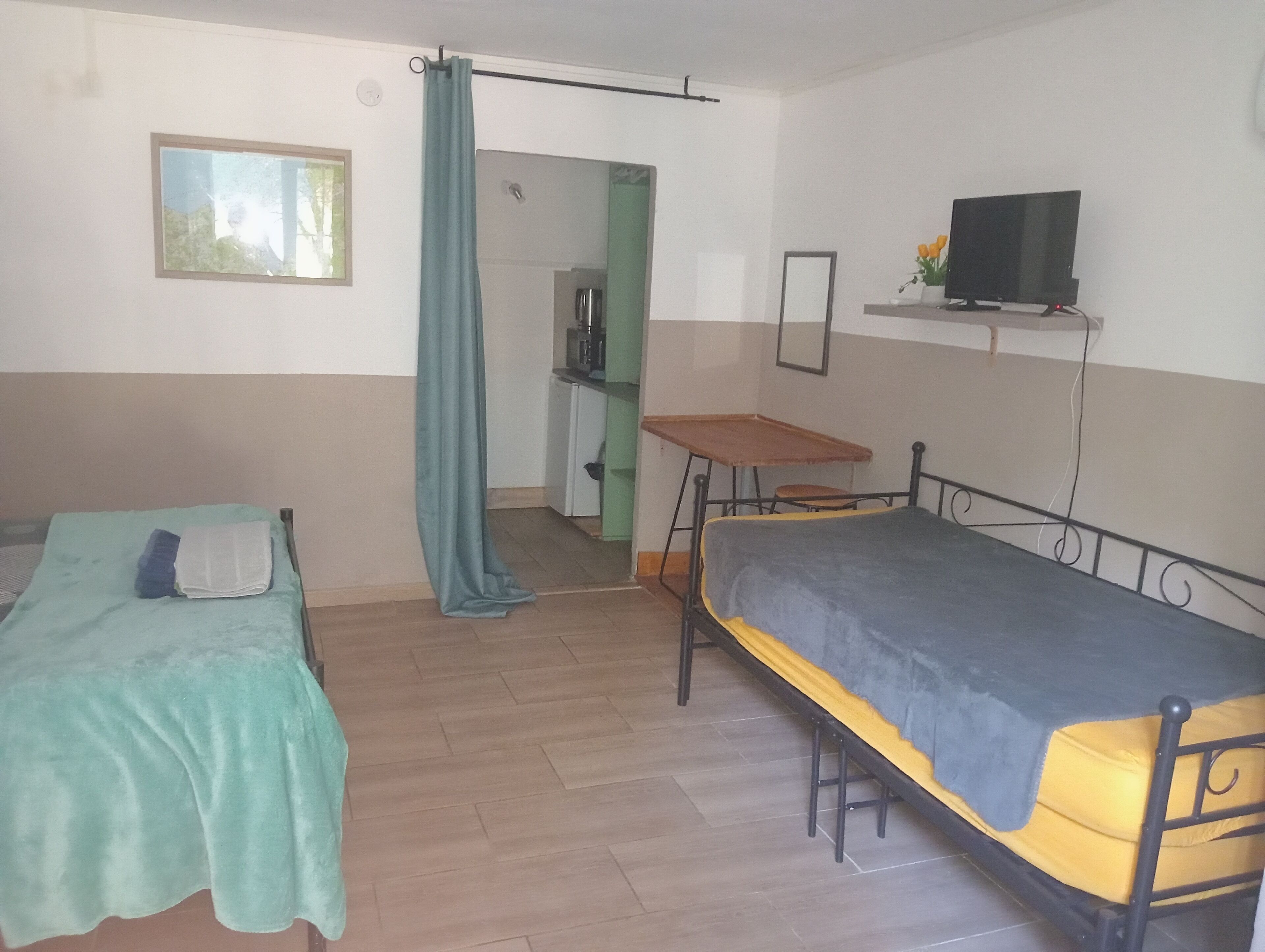 Una habitación pequeña y sencilla con dos camas individuales, una mesita, un televisor y una puerta que da a un rincón americano.