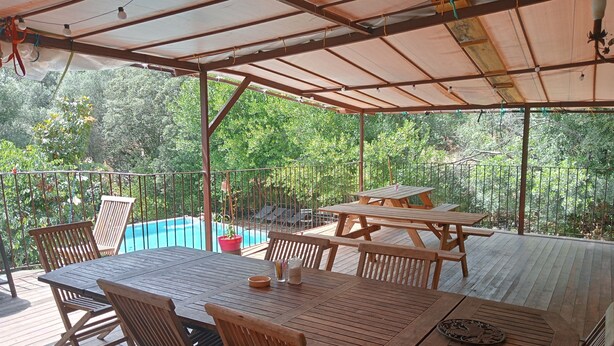 Un patio al aire libre con mesas y sillas de madera, una piscina y vistas a vegetación exuberante.