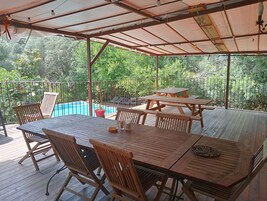 Un patio al aire libre con mesas y sillas de madera, una piscina y vistas a vegetación exuberante.