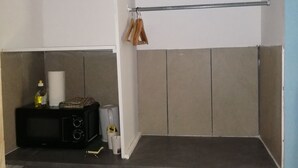 Una pequeña cocina americana con microondas, un refrigerador compacto, un estante con objetos colgando y un bote de basura.