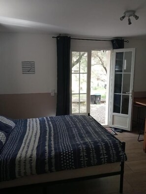 A room with a bed, a door leading to an outdoor area, and a small table. - Berbi Rosse (Oletta)