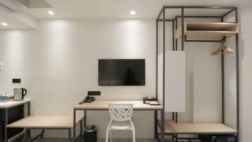 Habitación de hotel con escritorio, silla, televisor, armario y cama.