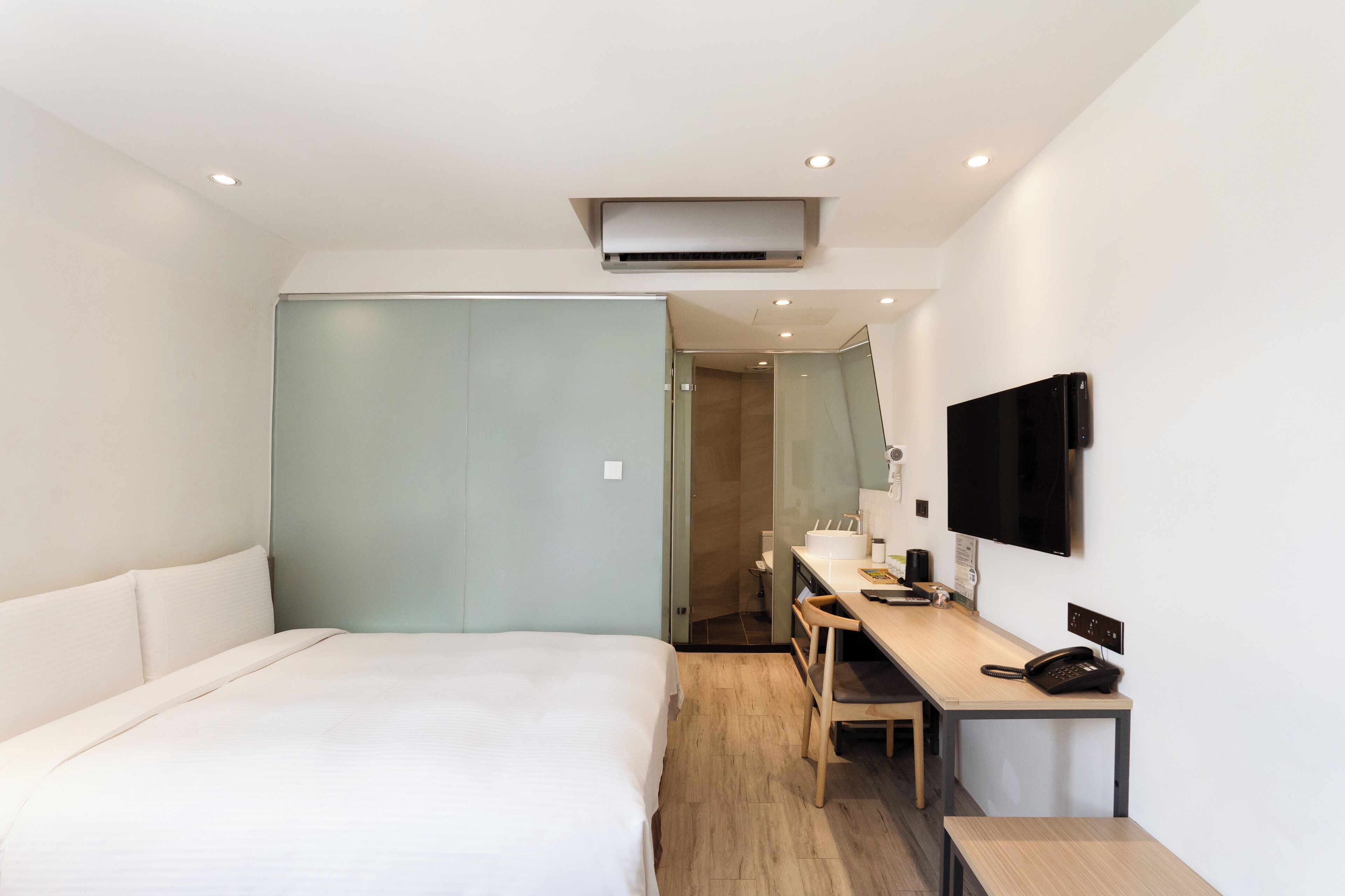 Ein modernes Hotelzimmer mit einem großen Bett, einem Schreibtisch mit Stuhl, einem Flachbildfernseher und einer integrierten Klimaanlage.