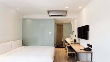 Ein modernes Hotelzimmer mit einem großen Bett, einem Schreibtisch mit Stuhl, einem Flachbildfernseher und einer integrierten Klimaanlage.