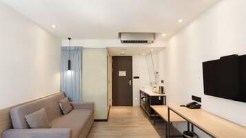 A modern hotel room with a sofa, a desk with a computer, a TV, and a door leading to another room.