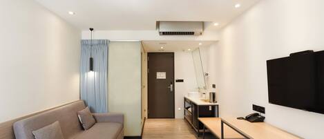 Une chambre d’hôtel moderne équipée d’un canapé, d’un bureau avec un ordinateur, d’une télévision et d’une porte donnant sur une autre pièce.
