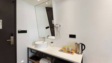 A modern bathroom with a white sink, a mirror, a hairdryer, a kettle, and a tray with toiletries.