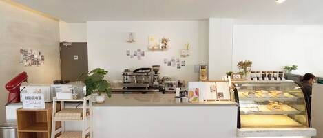 Una cafetería moderna con mostrador de mármol, máquinas de café y una vitrina con pasteles.