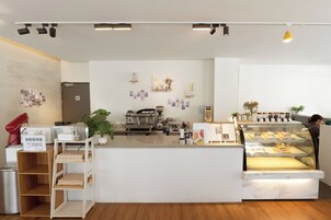 Una cafetería moderna con mostrador de mármol, máquinas de café y una vitrina con pasteles.