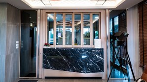 Uma área de recepção moderna com balcão de mármore, portas de vidro e teto com luminárias circulares.