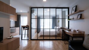 Quarto de hotel moderno com porta deslizante separando o quarto e a sala de estar. Inclui uma mesa, uma cadeira, uma TV e um sofá.