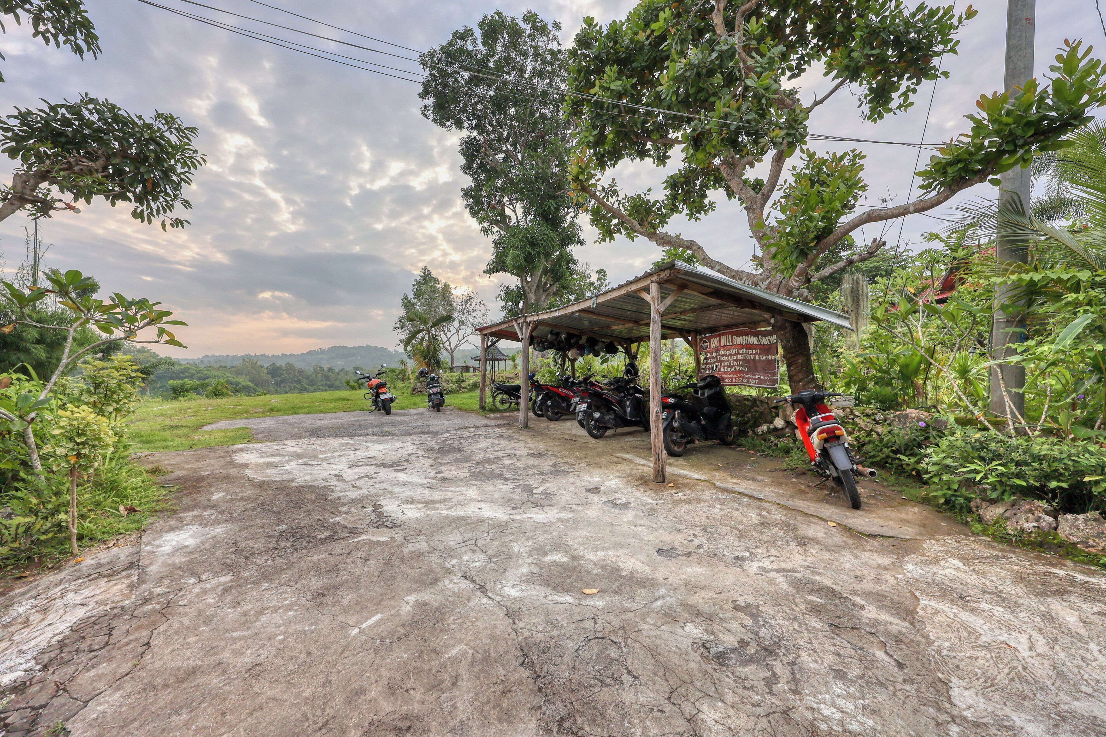 A concrete road leading to a covered parking area with motorcycles parked under a shelter, surrounded by greenery and trees.