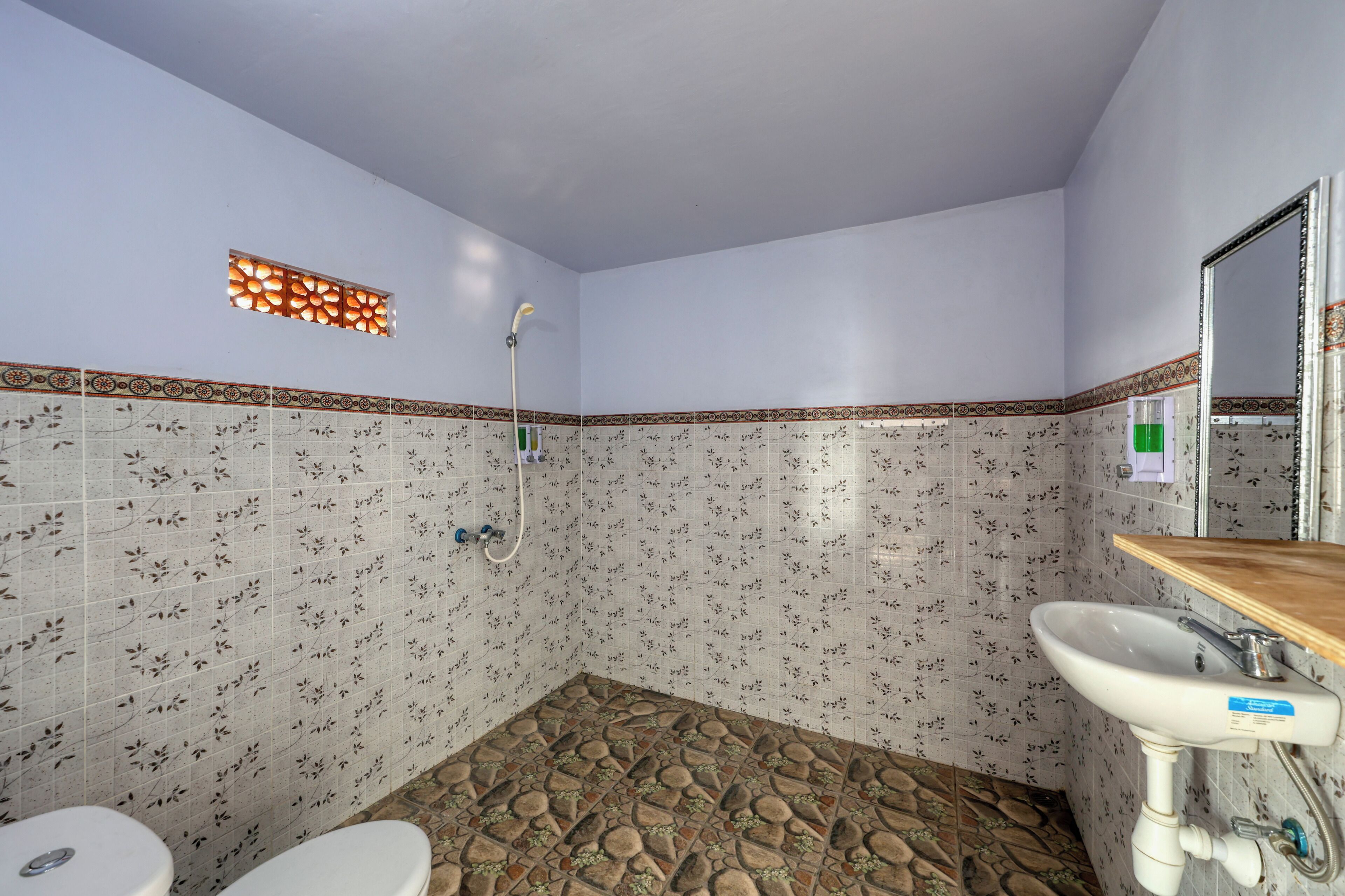 Un baño con ducha, inodoro y lavamanos, con azulejos estampados y suelo de piedra.