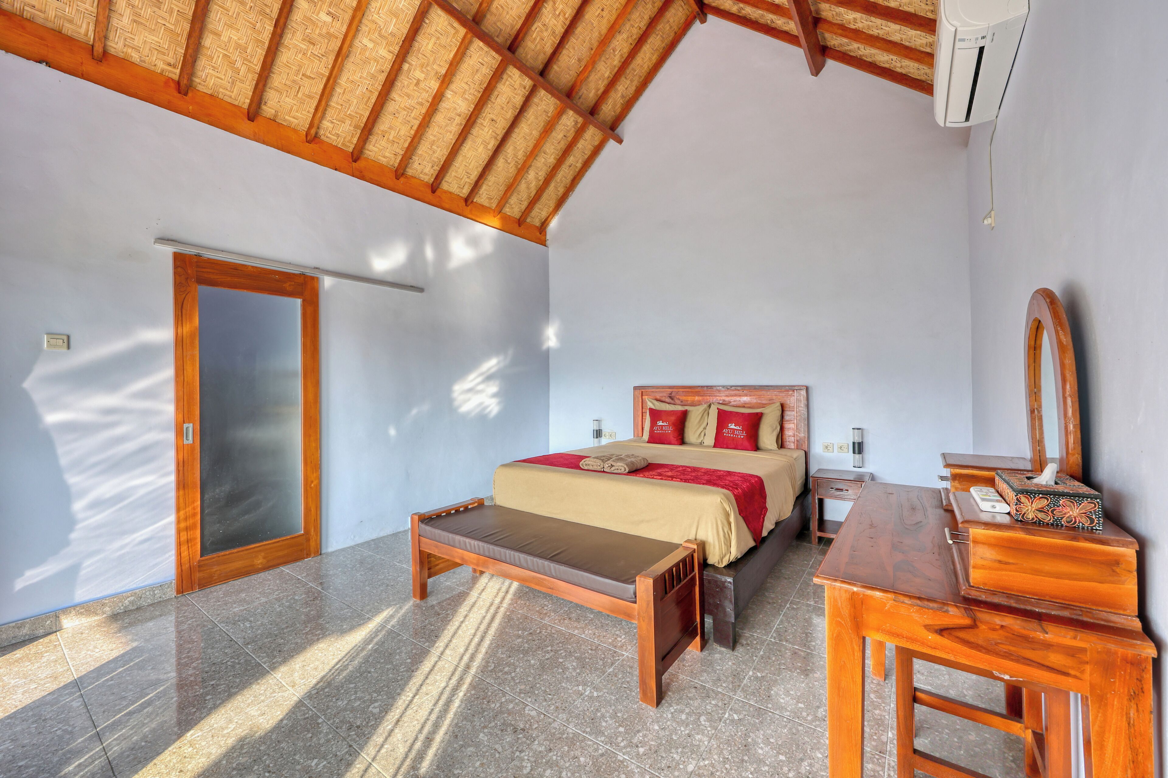 A bedroom with a bed, bedside table, bench, and a wooden desk with a mirror.