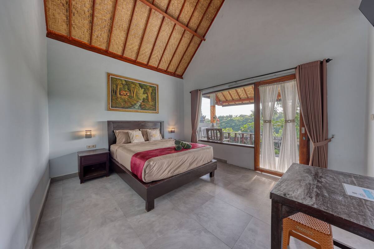 Een slaapkamer met een bed, nachtkastje en uitzicht door een raam.
